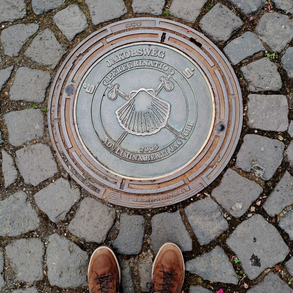 Kanaldeckel mit dem Zeichen des Jakobwegs in der Eifel